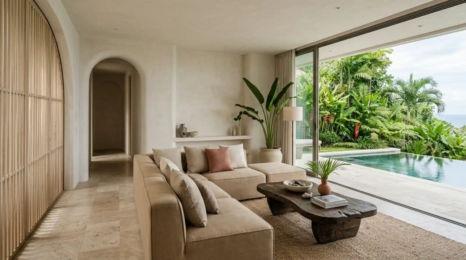 Tropical modern interior design in Bali — warm-minimalist living room with microcement walls, travertine floor and sliding doors open to the pool