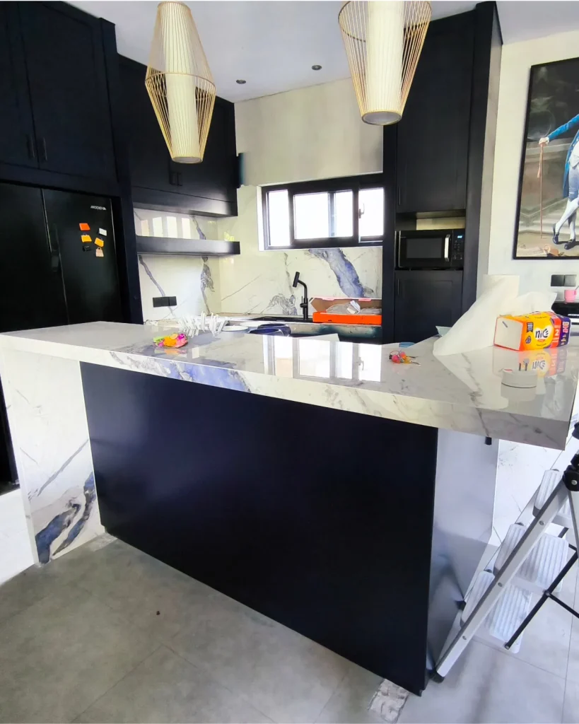 The same kitchen after redesign, with deep navy cabinetry, a bookmatched blue-marble splashback and blue LED accent lighting