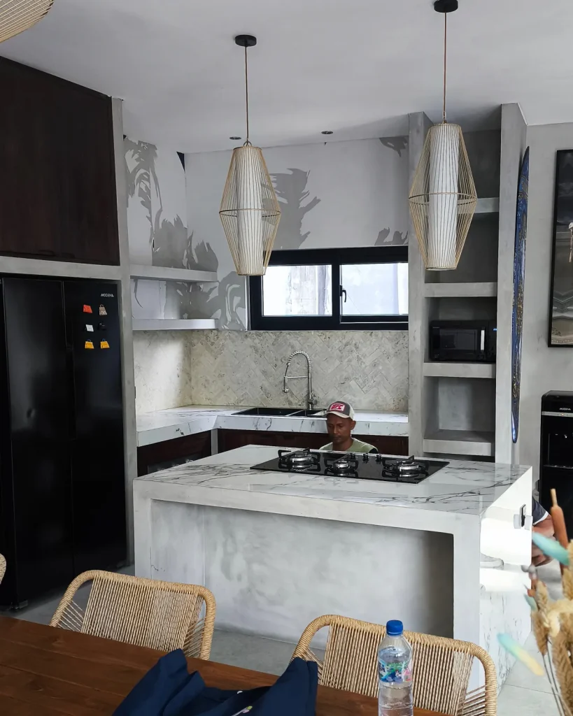 The Soho Blue villa kitchen before renovation: a raw grey polished-concrete island and shelving with a plain marble splashback