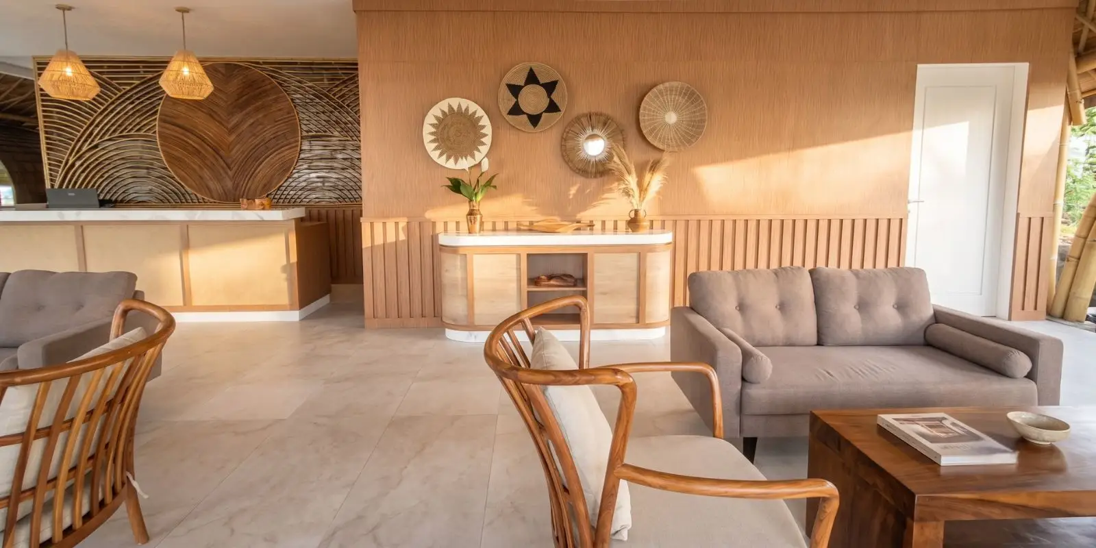 Tropical villa lounge with rattan armchairs, a grey linen sofa and cane-panelled joinery, woven wall baskets and travertine floors in a warm timber palette