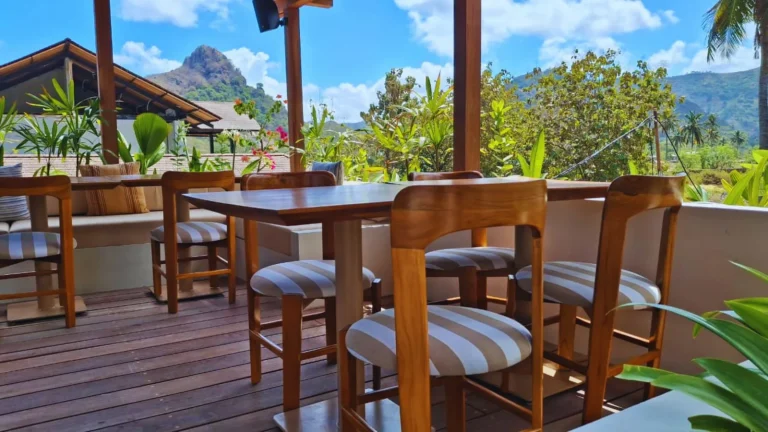 Custom teak dining chairs and tables on the open rooftop terrace at Boni Beach Lombok, with the south Lombok hills behind