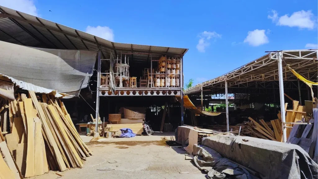 The Bali Best Design workshop in Kerobokan, with stacked timber stock, open sided production sheds and finished chairs and rattan stools on the mezzanine