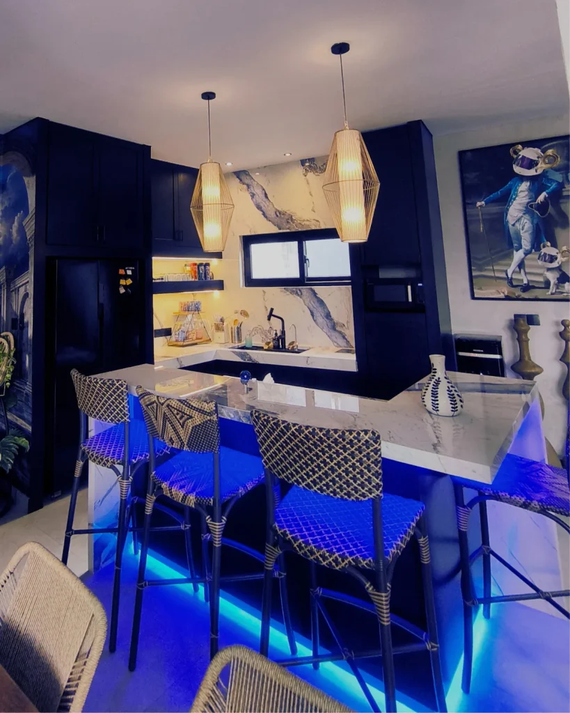 The completed Soho Blue villa kitchen seen from the dining area, with dark navy cabinetry, blue-veined marble and blue LED lighting under the bar counter