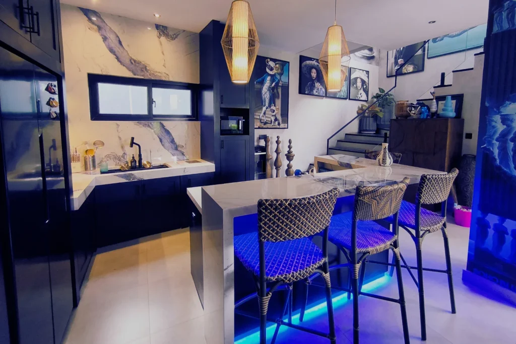 The bar counter in the completed Soho Blue villa kitchen, with woven rattan stools and a recessed blue LED strip lighting the marble counter