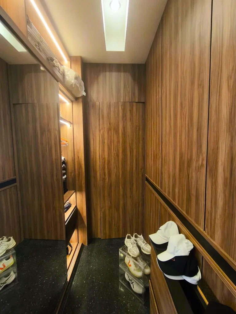 Walk-in wardrobe corridor in a Kerobokan master suite, Bali, with mirror-fronted sliding doors, LED-lit hanging rails and full-height walnut joinery, designed by Bali Best Design