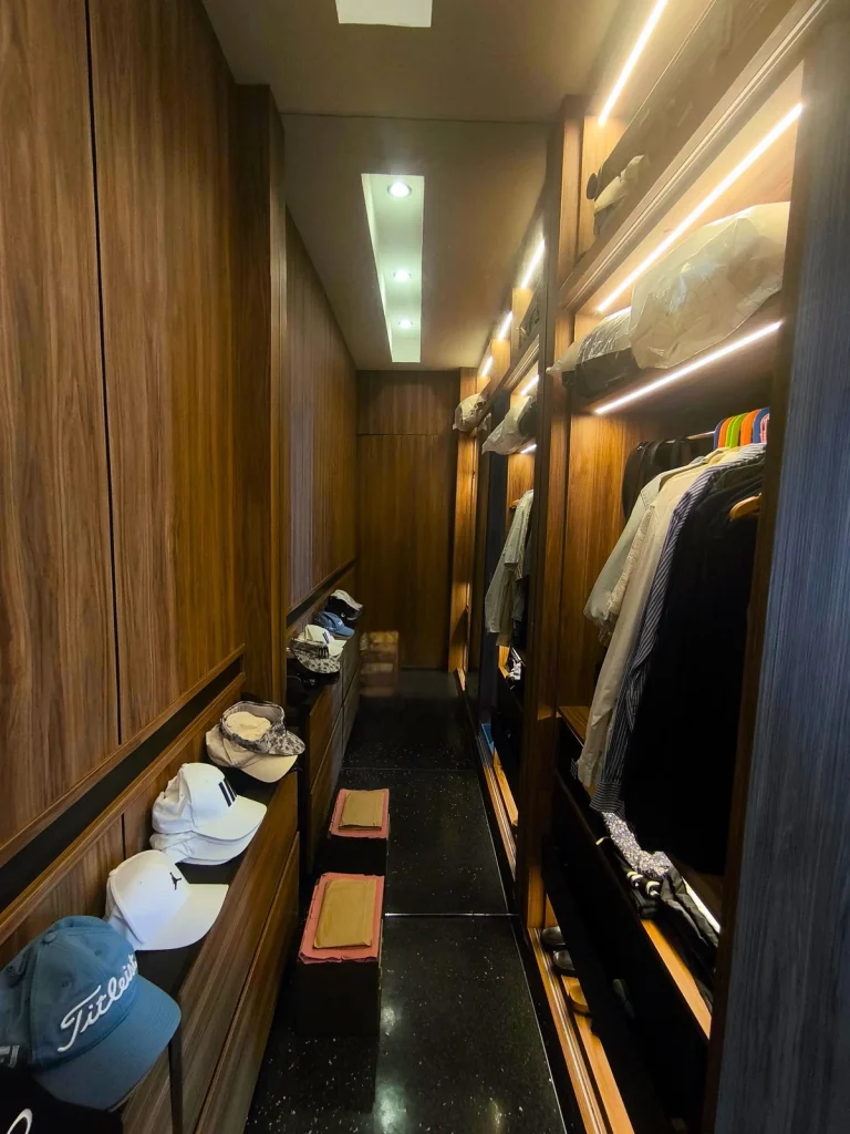 Walk-in wardrobe in a Kerobokan master suite, Bali, with backlit open hanging sections, closed walnut joinery with recessed black handle lines and a low drawer run, designed by Bali Best Design