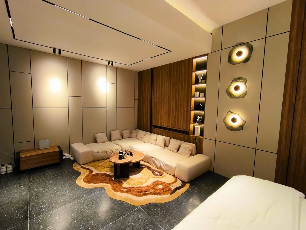 Master suite lounge in Kerobokan, Bali, with a cream modular sofa, an organic-edge rug, three sculptural shell wall lights and a backlit walnut display column, designed by Bali Best Design