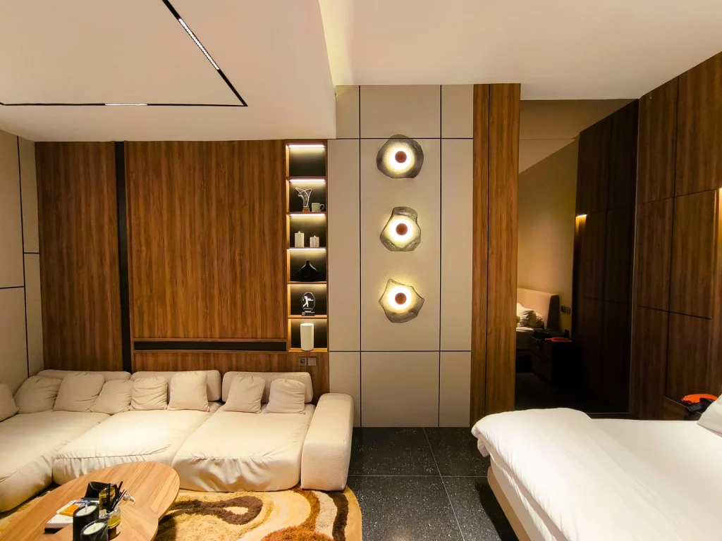Master suite lounge looking through to the bedroom in Kerobokan, Bali, with a walnut feature wall, backlit display niche and three sculptural shell wall lights, designed by Bali Best Design