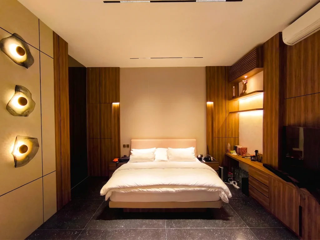 Master bedroom interior design in Kerobokan, Bali, with three sculptural shell wall lights, full-height walnut wardrobes, an upholstered headboard wall and dark terrazzo flooring, designed by Bali Best Design